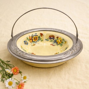 May include: A vintage yellow ceramic serving dish with a floral pattern and a silver-colored metal rim and handle. The dish features a decorative floral design in the center and is ideal for serving food or as a decorative piece.