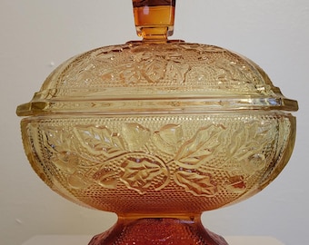 May include: A vintage glass candy dish with a lid. The dish is amber and clear glass with a floral pattern. The lid has a square knob.