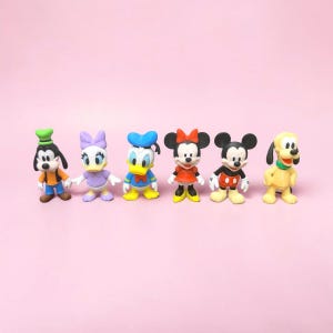May include: A set of six small cartoon character figurines standing in a row. The figures include Goofy in a green hat, Daisy Duck in a purple dress, Donald Duck in a blue sailor suit, Minnie Mouse in a red dress, Mickey Mouse, and Pluto.