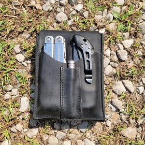 Pu&ograve; includere: Un astuccio in pelle nera con tre tasche. Un multiutensile argentato con la scritta "Leatherman" &egrave; nella tasca sinistra. Un coltello nero con manico argentato &egrave; nella tasca destra. Una penna argentata &egrave; nella tasca centrale.