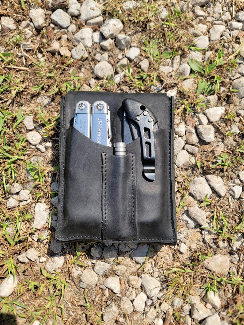 Pu&ograve; includere: Un astuccio in pelle nera con tre tasche. Un multiutensile argentato con la scritta "Leatherman" &egrave; nella tasca sinistra. Un coltello nero con manico argentato &egrave; nella tasca destra. Una penna argentata &egrave; nella tasca centrale.