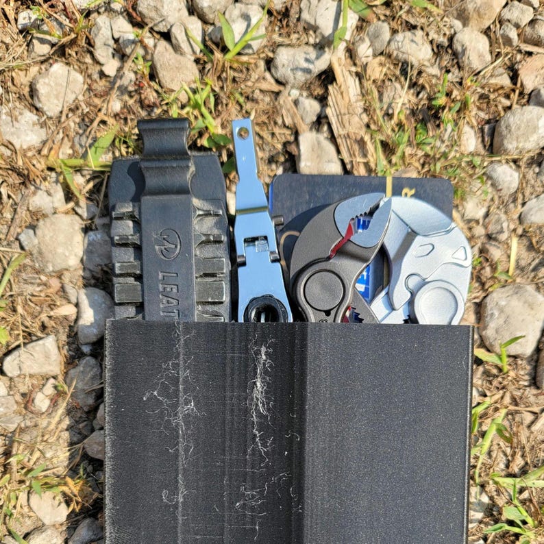 Pu&ograve; includere: Una custodia nera multi-utensili con una variet&agrave; di strumenti, tra cui un multi-utensili Leatherman, un paio di pinze e un piccolo cacciavite. La custodia &egrave; realizzata in un materiale resistente e ha una chiusura a zip.