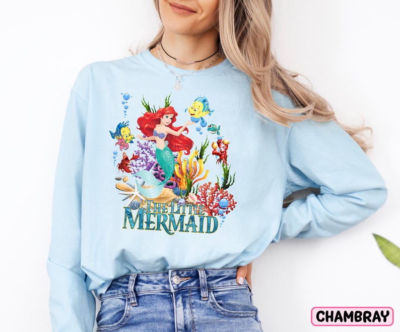 a woman wearing a light blue sweatshirt with the words mermaid printed on it