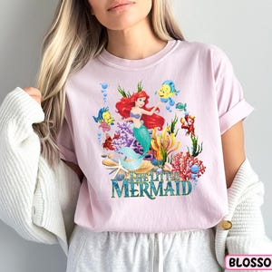 a woman wearing a pink shirt with a mermaid on it