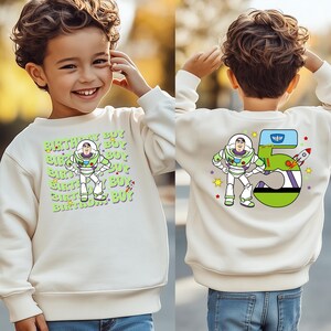 a young boy wearing a white sweatshirt with an astronaut on it
