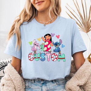 A woman wearing a light blue t-shirt with a colorful graphic design featuring characters from the Disney animated film "Stitch".