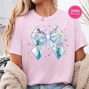 A woman wearing a pink t-shirt with a large bow featuring illustrations of characters from the Disney movie Frozen.