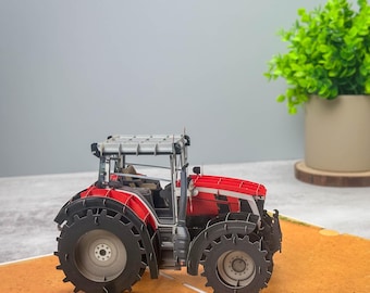 May include: A red and gray pop-up card featuring a detailed model of a tractor. The tractor has large black wheels and a gray cab.
