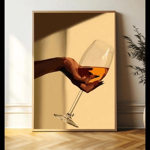 May include: A framed art print featuring a hand holding a wine glass filled with amber liquid. The artwork has a minimalist style with a warm color palette, including shades of brown and yellow. The glass is clear, and the background is a solid color.