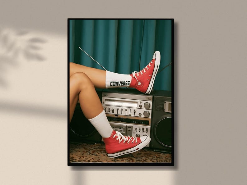 May include: A woman wearing red Converse sneakers with white socks. The socks have the word "Converse" written on them. The woman is sitting on a vintage stereo system with a microphone.