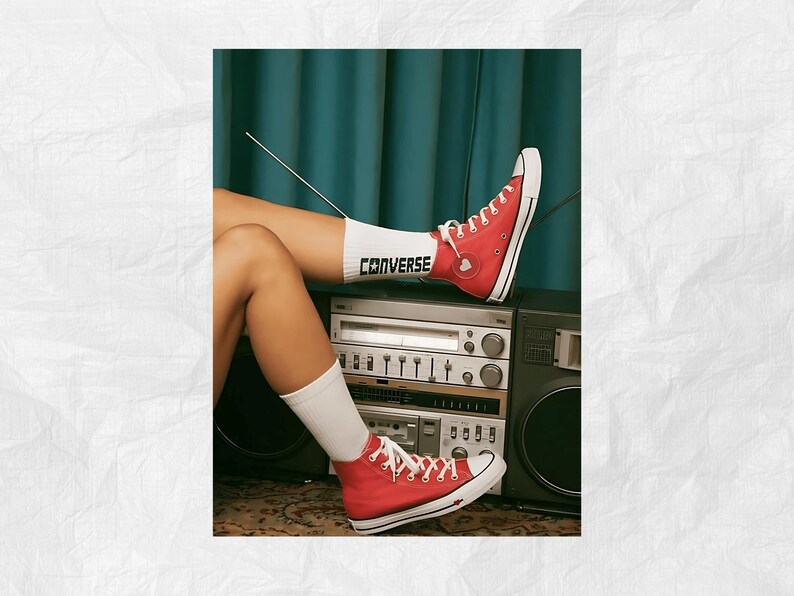 May include: Red high-top Converse sneakers with white laces and a white sock with the word "CONVERSE" printed on it. The sneakers are worn by a person sitting on a vintage stereo system.