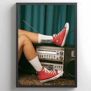 May include: A woman's legs are resting on a vintage stereo system. She is wearing red Converse sneakers with white socks that say "Converse" on them. The stereo has a cassette player, a tuner, and a record player.