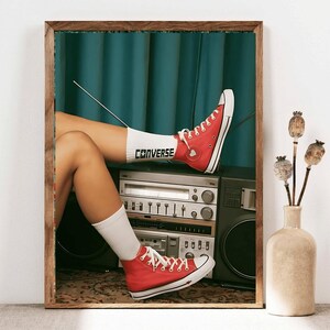 May include: A vintage-style boombox with a red Converse shoe resting on top. The shoe has a white sock with the word "Converse" written on it. The boombox is sitting on a patterned rug.