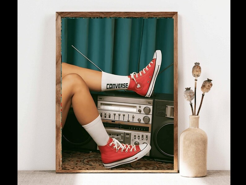 May include: A vintage-style boombox with a red Converse shoe resting on top. The shoe has a white sock with the word "Converse" written on it. The boombox is sitting on a patterned rug.