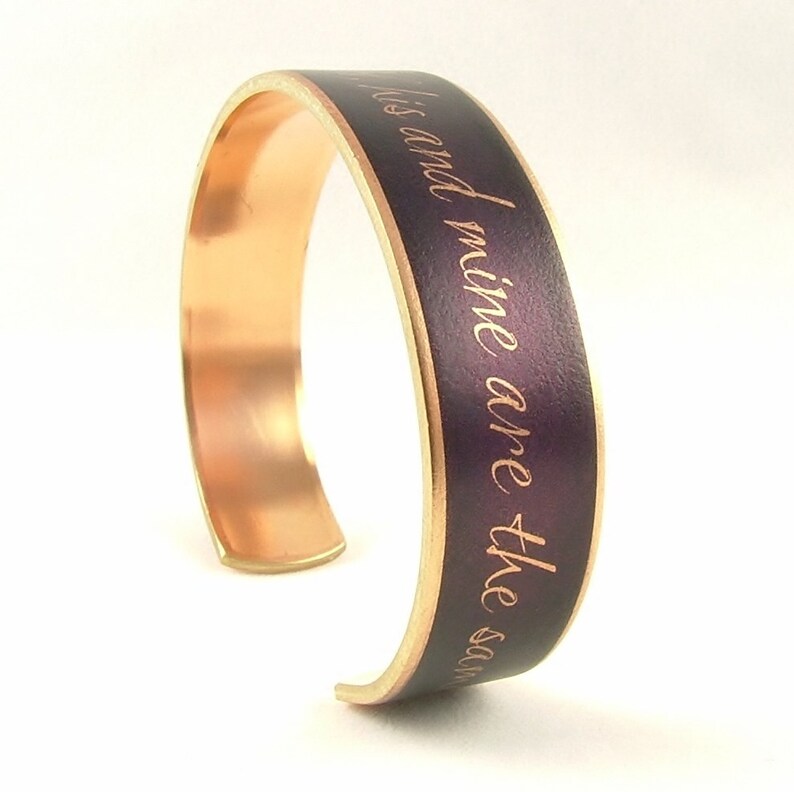 May include: A copper cuff bracelet with a purple enamel band. The band has the words "His and mine are the same" engraved in gold.