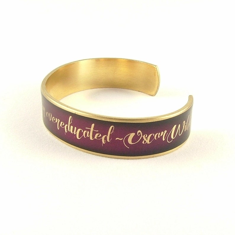 May include: Gold-toned bangle bracelet with a dark purple enamel band and the inscription "I am never educated" - Oscar Wilde in gold lettering.