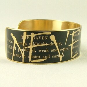 May include: A gold metal bracelet with a black background and gold lettering. The text reads "THE RAVEN. ONCE upon a midnight dreary, While I pondered, weak and weary, Over many a quaint and curious As of"