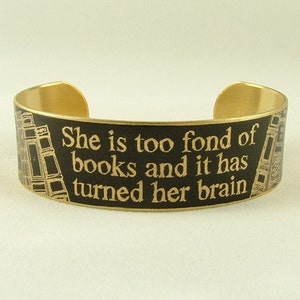 K&ouml;nnte beinhalten: Ein goldfarbenes Metallarmband mit schwarzem Hintergrund und goldener Aufschrift "She is too fond of books and it has turned her brain".