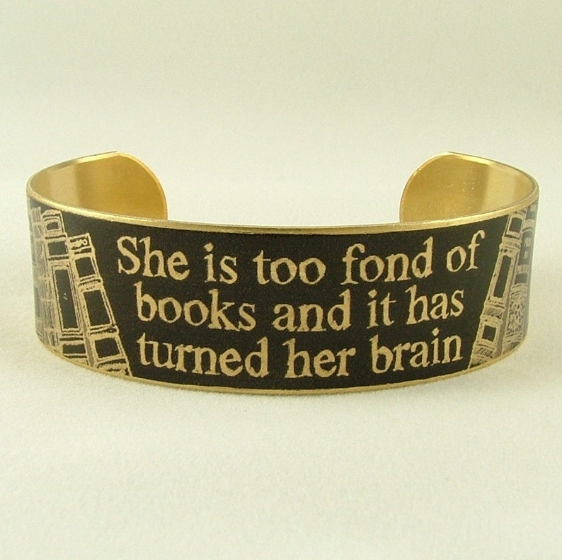 K&ouml;nnte beinhalten: Ein goldfarbenes Metallarmband mit schwarzem Hintergrund und goldener Aufschrift "She is too fond of books and it has turned her brain".