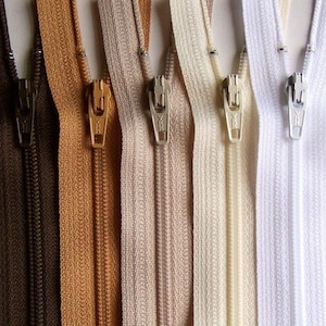 May include: Six different colors of zipper tape, including brown, tan, beige, cream, and white. The zippers are all closed and have a metal slider.