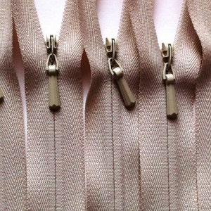 Op de afbeelding: Vier beige ritsluitingen met een chevron-patroon en beige ritsjes.