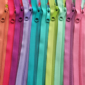 May include: A close-up of a variety of colourful zipper tapes. The zippers are arranged in a row, with the slider ends facing the viewer. The colours include red, purple, lavender, teal, green, and pink.