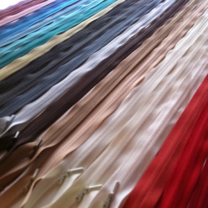 May include: A selection of zipper tapes in various colours, including red, white, beige, brown, grey, teal, blue, and purple. The zipper tapes are laid out in rows, with the red zipper tape at the bottom.