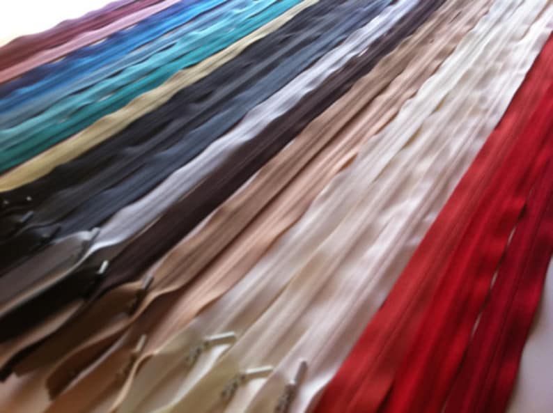 May include: A selection of zipper tapes in various colours, including red, white, beige, brown, grey, teal, blue, and purple. The zipper tapes are laid out in rows, with the red zipper tape at the bottom.