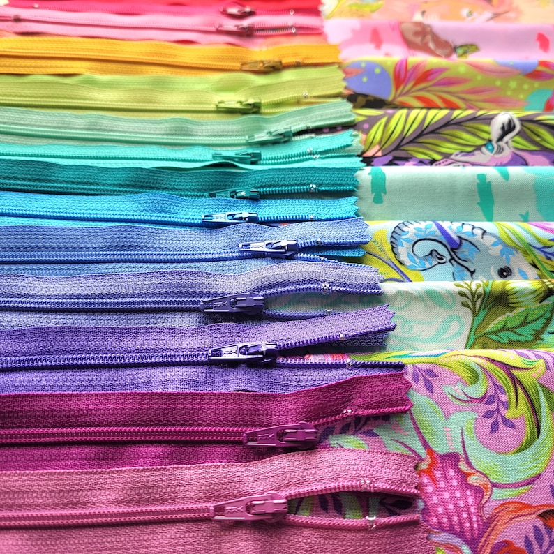 May include: A rainbow assortment of colourful zippers arranged in a vertical stack. The zippers are arranged from red to purple, with each colour having a different shade. The zippers are all closed and have a metal slider.