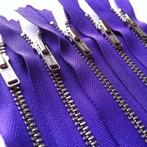 Op de afbeelding: Een verzameling van vijf paarse ritsen die parallel zijn gerangschikt. Elke rits is voorzien van een zilverkleurige metalen schuiver en treklipje met een zichtbaar YKK-logo. Het stoffen band is felpaars en de tandjes zijn van zilverkleurig metaal.