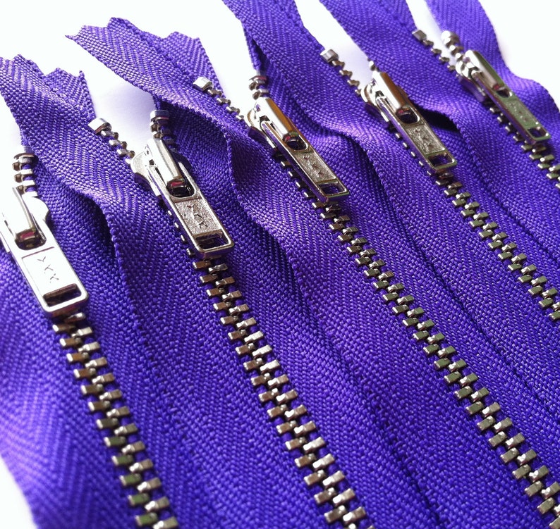Op de afbeelding: Een verzameling van vijf paarse ritsen die parallel zijn gerangschikt. Elke rits is voorzien van een zilverkleurige metalen schuiver en treklipje met een zichtbaar YKK-logo. Het stoffen band is felpaars en de tandjes zijn van zilverkleurig metaal.