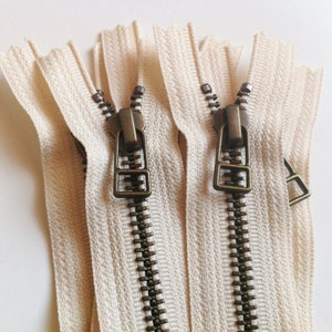 May include: Three off-white zipper tapes with antique brass zipper pulls. The zipper teeth are metal and have a dark brown finish.
