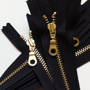 May include: Two black zipper tapes with gold metal teeth and sliders. The sliders have the YKK logo on them.