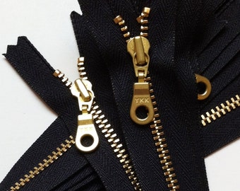 May include: Two black zipper tapes with gold metal teeth and sliders. The sliders have the YKK logo on them.