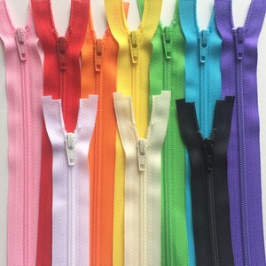 Puede incluir: Una colecci&oacute;n de 12 cierres de cremallera en varios colores, incluyendo rosa, rojo, blanco, naranja, amarillo, verde, azul, negro y morado. Las cremalleras est&aacute;n todas cerradas y dispuestas en una fila.