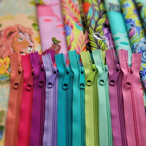 May include: A close-up of a variety of colourful zipper pulls. The zippers are arranged in a row, with the colours ranging from brown to pink, purple, teal, green, and light blue.