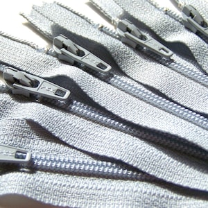 May include: A close-up of several silver zipper closures. The zippers are arranged in a fan shape, with the teeth of the zippers facing the viewer.