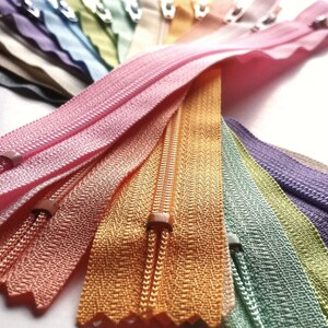 May include: A collection of colorful zipper tapes in various shades of pink, orange, green, purple, and blue. The zippers are arranged in a fan shape, showcasing the different colors and textures.