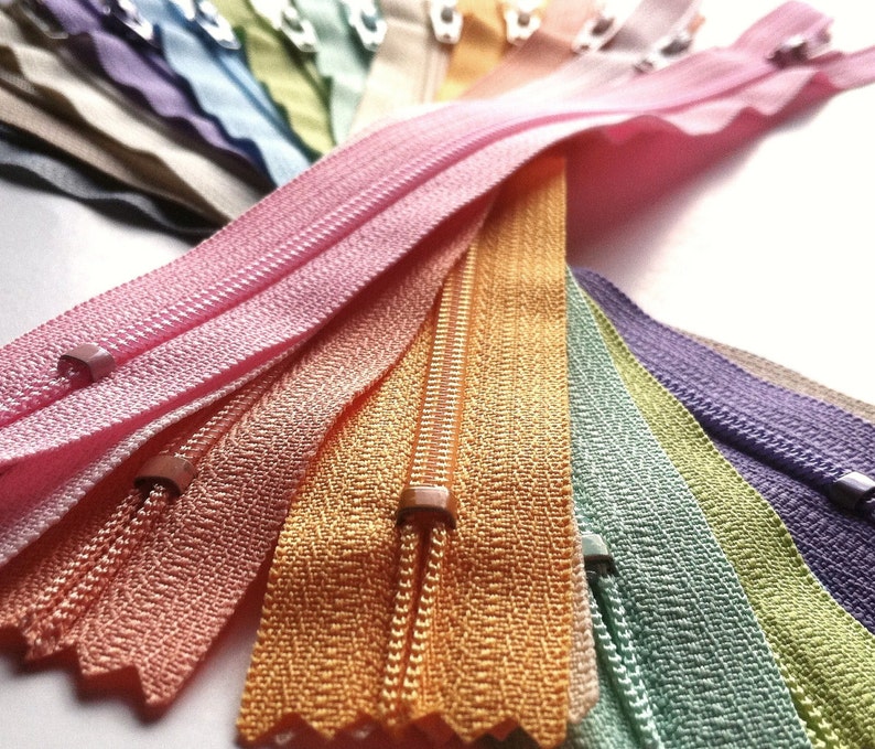 May include: A collection of colorful zipper tapes in various shades of pink, orange, green, purple, and blue. The zippers are arranged in a fan shape, showcasing the different colors and textures.