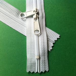 May include: White zipper with a white slider and a YKK logo. The zipper is on a green background.