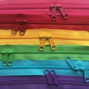 May include: Assortment of colorful zipper tapes with metal zipper pulls. The zipper tapes are red, yellow, green, blue, and purple. The zipper pulls are silver.