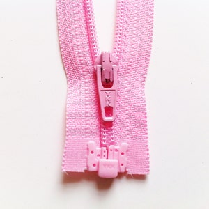 Op de afbeelding: Een roze rits met een roze schuif en een roze treklip. De rits is gesloten en de treklip bevindt zich bovenaan.