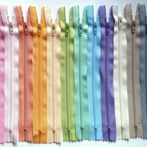 May include: A collection of 15 zipper tapes in various pastel colors, including pink, white, peach, orange, yellow, green, blue, purple, and beige. The zippers are all the same size and have a smooth, even texture.