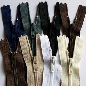 May include: Assortment of ten zipper closures in various colors, including navy blue, dark green, black, brown, beige, and white. The zippers are all open and have a metal slider.