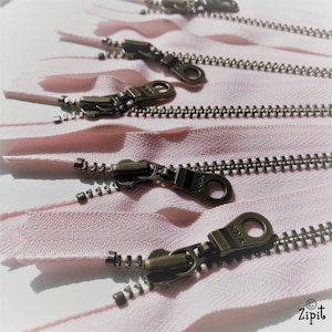 May include: A close-up of several pink zipper tapes with antique brass zipper pulls. The zipper teeth are silver.