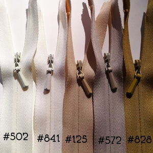 May include: Five zipper tapes in different colors: white, beige, light gray, and gold. The zipper tapes are labeled with numbers: #502, #841, #125, #572, and #828.