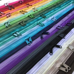 May include: A collection of colorful zipper tapes with different colored sliders. The zipper tapes are arranged in a rainbow pattern, with the darkest colors at the bottom and the lightest colors at the top.