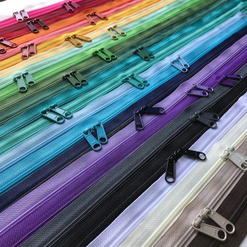 May include: A collection of colorful zipper tapes with different colored sliders. The zipper tapes are arranged in a rainbow pattern, with the darkest colors at the bottom and the lightest colors at the top.