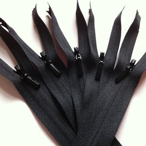 May include: Close-up of several black zippers with black pulls. The zippers are arranged in a fan shape, with the zipper teeth visible. The background is a plain white surface. These zippers are suitable for sewing projects.