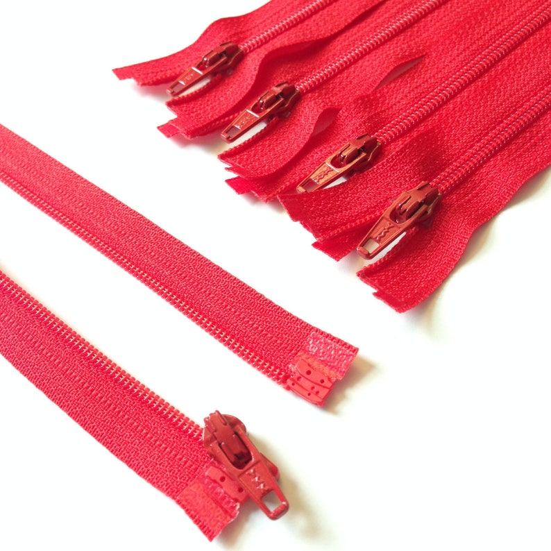 Puede incluir: Primer plano de una cinta de cremallera roja con un deslizador de metal rojo. La cinta de cremallera est&aacute; separada en dos piezas, una con el deslizador y la otra sin.